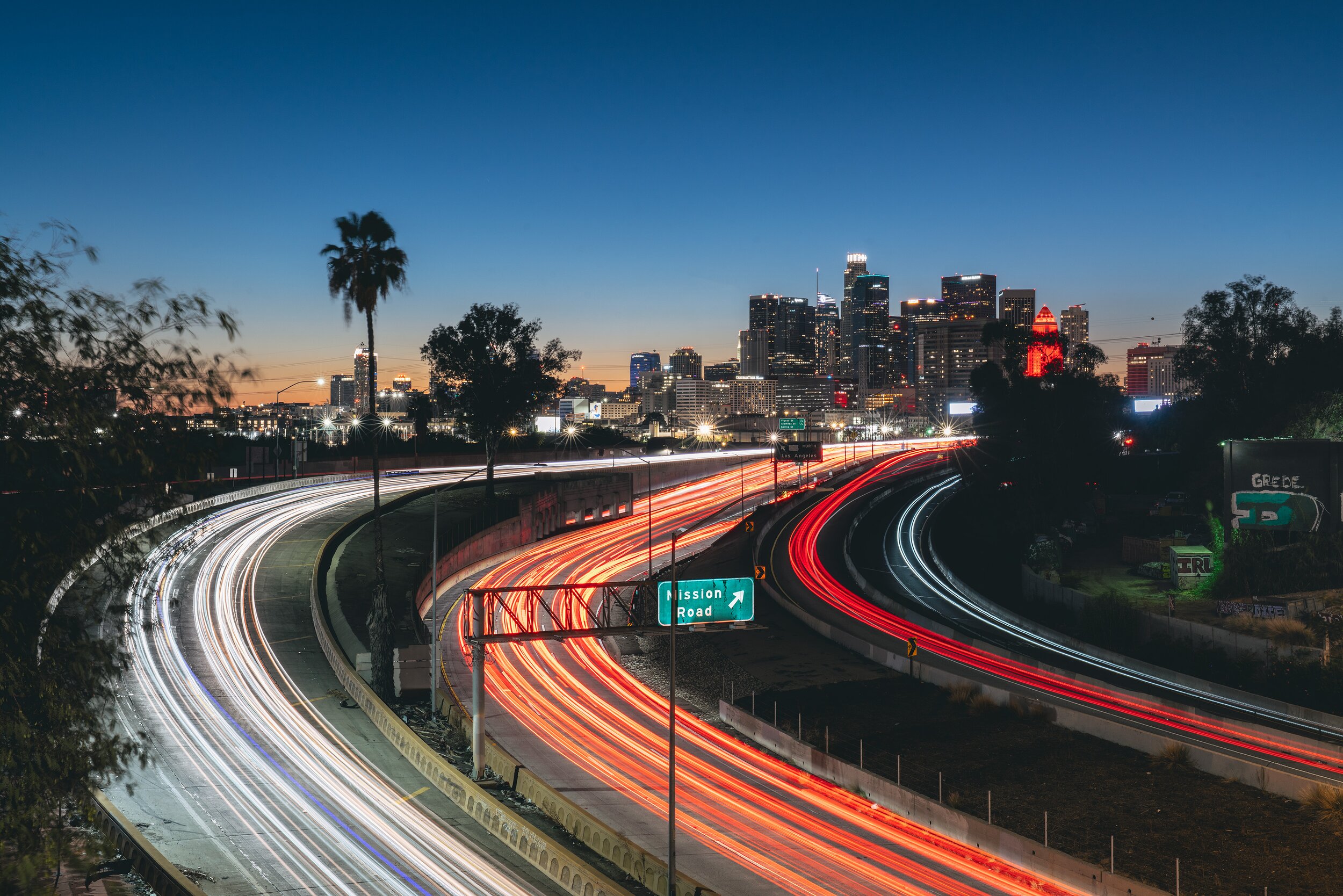 Freeway traffic light trails leading toward the downtown Los Angeles skyline at dusk
